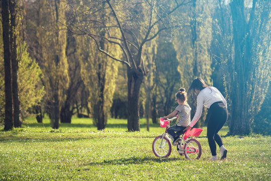 learning to ride a bicycle, young mom teaches her daughter to ride a bike
