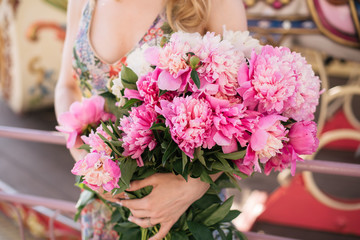 Beautiful girl in a dress with a bouquet of pink peonies in the hands near a vintage carousel