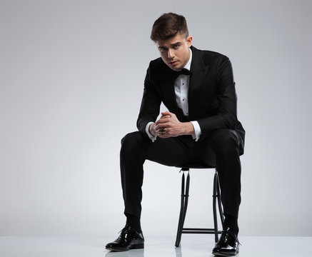 sexy young man in black tuxedo sitting on chair
