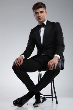 handsome man in tuxedo resting on metal chair