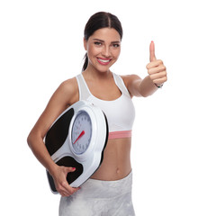 portrait of fit woman holding scale and making ok sign