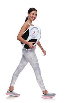 happy beautiful woman walking to side while holding scale