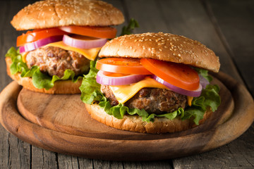 Close-up photo of home made hamburger with beer made of beef, onion, tomato, lettuce, cheese and spices. Fresh burger closeup on wooden rustic table with potato fries and chips.
