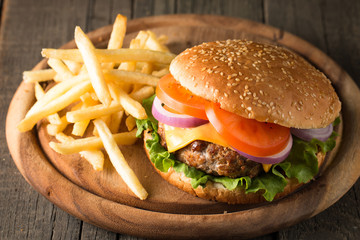 Close-up photo of home made hamburger with beer made of beef, onion, tomato, lettuce, cheese and spices. Fresh burger closeup on wooden rustic table with potato fries and chips.