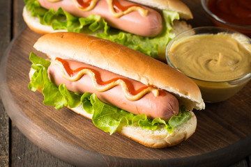 Tasty barbecue grilled hot dog with salad,yellow mustard, onion, ketchup, and French fries on wooden background. Junk and fast food concept.