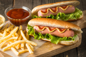 Tasty barbecue grilled hot dog with salad,yellow mustard, onion, ketchup, and French fries on wooden background. Junk and fast food concept.