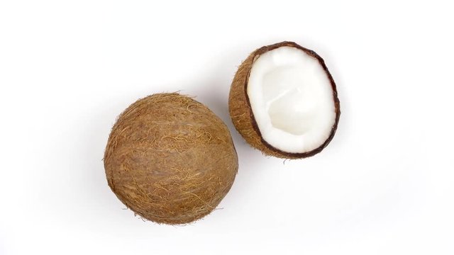 Top view of one whole ripe brown tropical coconut and a half with yummy white pulp rotating on white isolated background. Healthy fresh tropical fruits. Loopable seamless cocos rotating