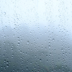 Rain drops on window glasses surface with cloudy and green background .
