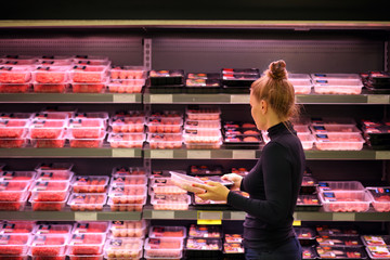 Woman purchasing a packet of meat at the supermarket - Powered by Adobe
