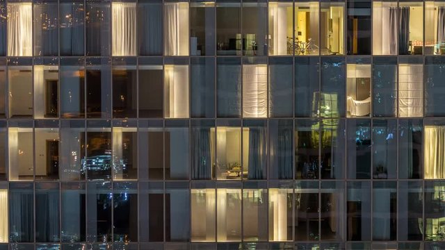 Windows of the multi-storey building of glass and steel lighting inside and moving people within timelapse