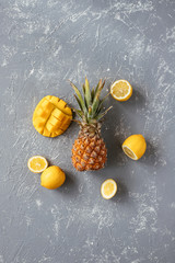 Yellow fruits. Ripe juicy pineapple with mango and lemons on gray wooden table, top view