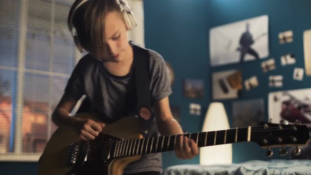 Expressive teen boy learning guitar play while standing in bedroom and playing with passion