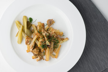 Fried potatoes with mushrooms, parsley and pickles on round plate. top view