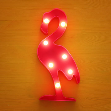 a plastic flamingo lamp with leds over yellow wooden background. holiday summer concept.