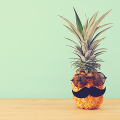 Pineapple on wooden table with funny moustache and sunglasses. Beach and tropical theme.