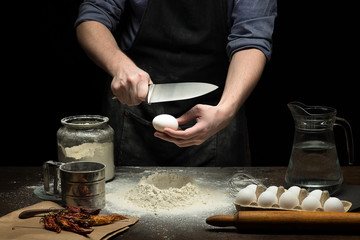 Hands are breaking an egg into flour to make dough on wooden table