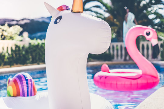 Inflatable colorful white unicorn and pink flamingo at the swim pool. Holidays time in the swimming pool with plastic toys. Relaxation and fun concept