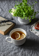 Lemon tea, book, mint flower pot on grey table. Cozy home still life