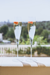 Two champagne glasses with strawberry on sunny terrace outdoor patio overlooking green trees at summer day outside of the city.Vertical