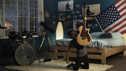 Teen boy in headphones jumping on bed in bedroom and playing guitar in dreams of being rock star in future