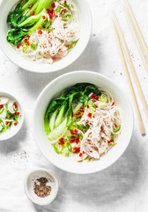 Chicken broth with rice noodles, boiled chicken, cabbage bok choi, spices on white background, top view. Asian style food
