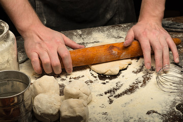 Chef hands are rolling dough on wooden table with wheat flour. close-up