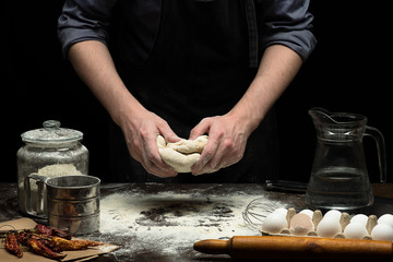 Hands are kneading the dough on wooden table and black background