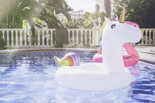 Inflatable colorful white unicorn and pink flamingo at the swim pool. Summer time in the swimming pool with plastic toys. Relaxation and fun concept