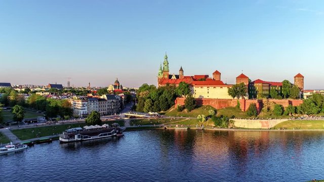 Krakow, Poland. Wawel royal Castle and Cathedral, Vistula River, park, harbor, walking people and a flying seagull. Cracow old city in the background. Aerial 4K reveal video at sunset in spring