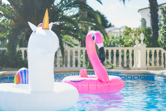 Inflatable colorful white unicorn and pink flamingo at the swim pool. Holidays week in the swimming pool with plastic toys. Relaxation and fun concept