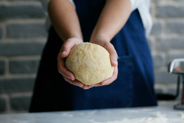 chef holding a ball of dough later to become pasta noodles, wearing a blue apron and standing...