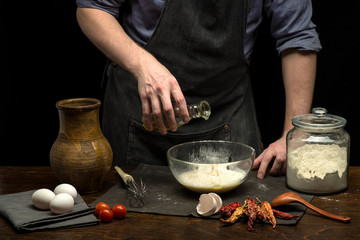 Chef hands are pouring oil into glass bowl to prepare dough. Black background