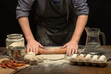 Chef hands are rolling a dough to make pizza on wooden table