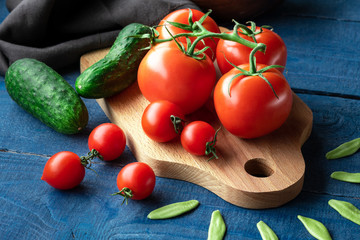 Tomatoes and cucumbers on wooden board with raw pasta on blue background