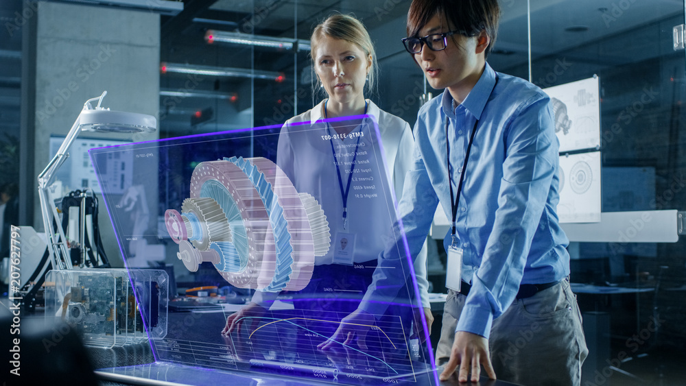 Wall mural male and female engineers have discussion while using modern computer with transparent holographic d