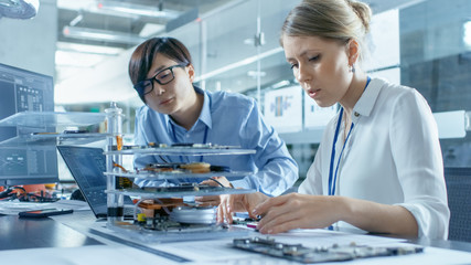 Obraz premium Two Computer Engineers Choose Printed Circuit Boards to Work with. In The Background Technologically Advanced Scientific Research Center.