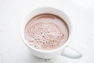 Cocoa drink with bubbles in a white mug on the table.