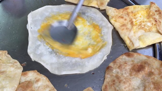 Cooking exotic Thai pancakes, malaysian roti with different stuffing on a  market in Thailand. making eggs roti roll on hot metal pans with boiled oil. street food Food of Thailand. Thai Dessert.