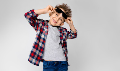 A handsome boy in a plaid shirt, gray shirt and jeans stands on a gray background. The boy in black...
