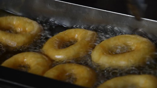 Close up deep frying several small round ring donuts in sizzling oil, high angle view