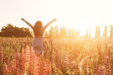 Happy woman in green flower field raised hands to sky. Warm soft sunset light