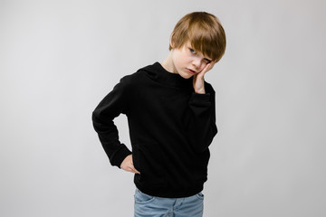 Fototapeta premium Charming teenager with blond hair and dark eyes. The teenager propped his cheek with his fingers. The teenager is displeased