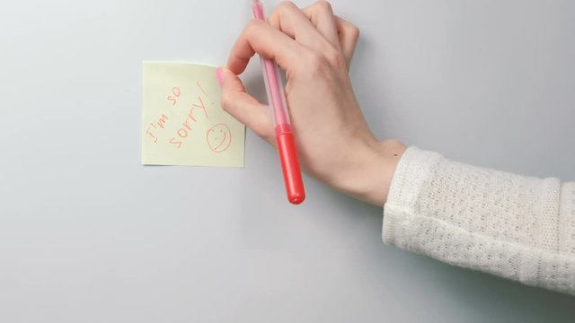 Closeup woman's hands stick yellow sticker paper sheets with words i'm so sorry. Family note.