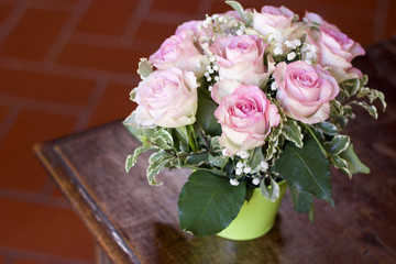 bouquet of pink roses in a small green jar on wooden furniture