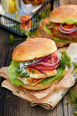 Vegetarian burger with grilled halloumi cheese, fresh lettuce, tomato, cucumber and onion with the addition of yoghurt mint sauce on a wooden rustic table, close up