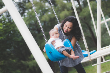 mother playing swing with  baby on  playground.