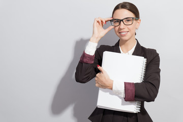 Young smiling businesswoman in glasses holding books in her hands. Fashion style photoshoot with har light source