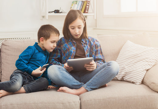 Two kids with gadgets on couch at home