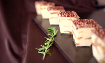row of tiramisu glasses on a dark wooden background decorated with a branch of rosemary