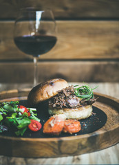 Pulled pork meat burger with vegetables and glass of red wine, wooden wall background, copy space © sonyakamoz